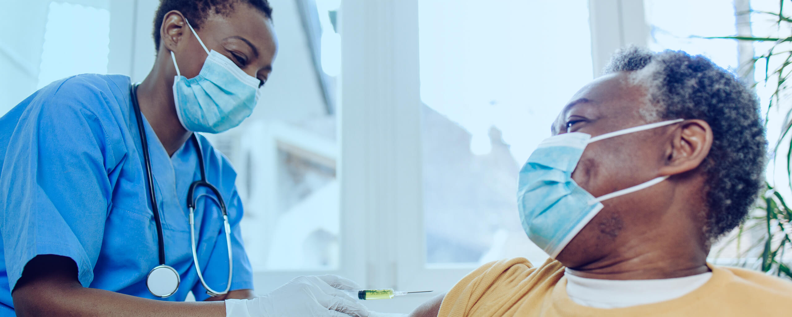 A nurse wearing a surgical mask administers a shot into the arm of a patient