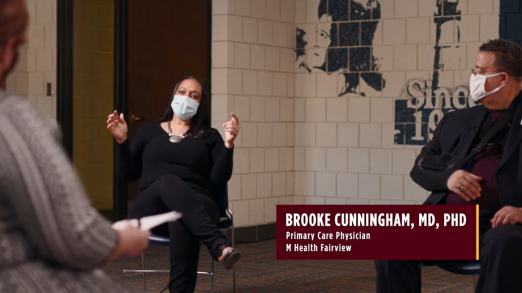 Image of Black woman and Black man sitting in chairs several feet apart wearing masks. The woman is identified as Brooke Cunningham, MD, PhD, primary care physician with M Health Fairview.