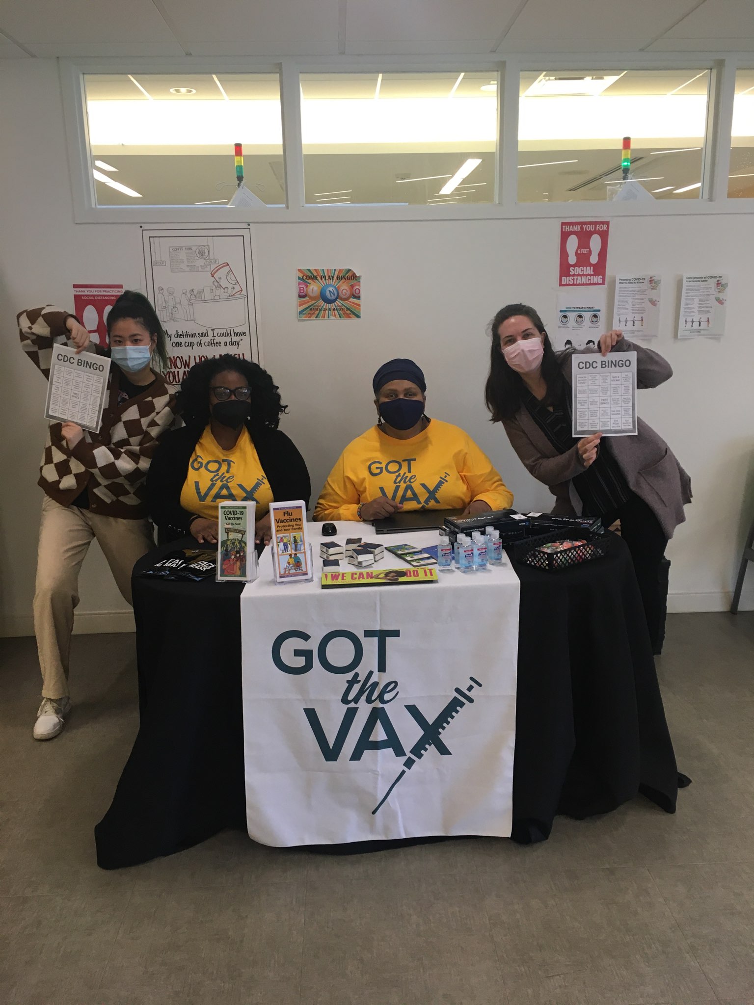 Volunteers pose behind a "Got the Vax" table showing off CDC Bingo cards