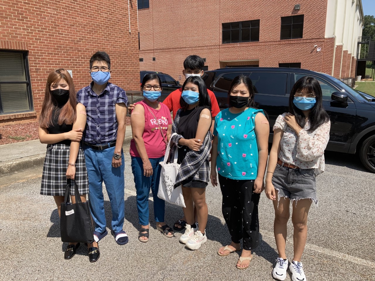 A family wearing masks poses together and shows off vaccination bandages