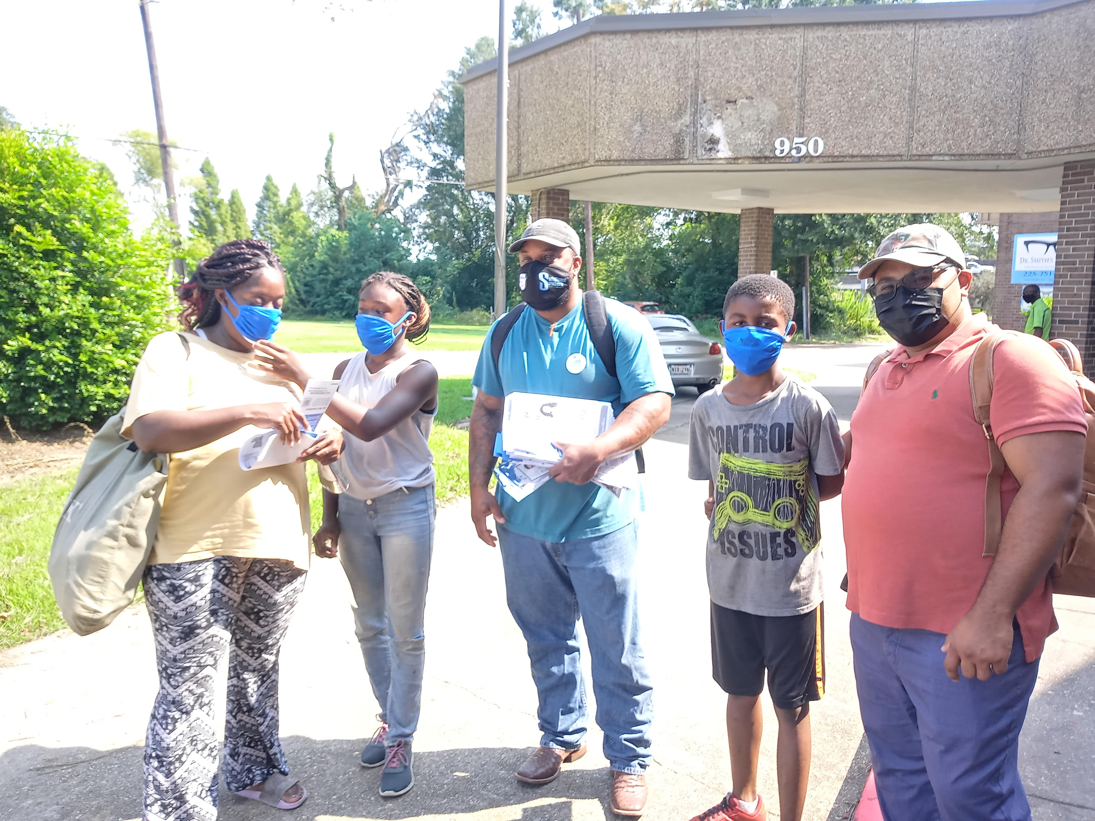 A group of people wearing masks and holding flyers pose for a picture