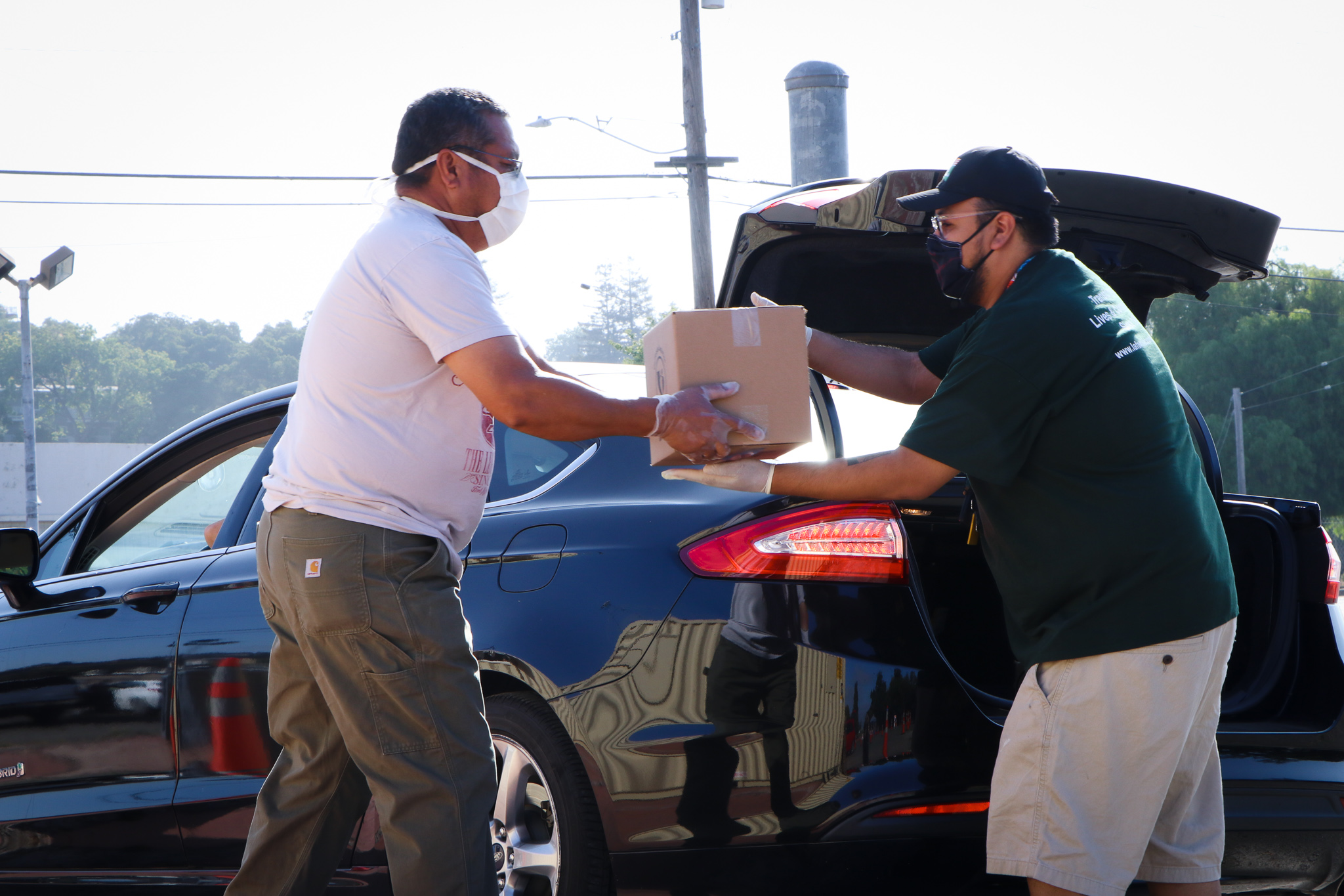 Two Hispanic men wearing masks hand a box off to once another