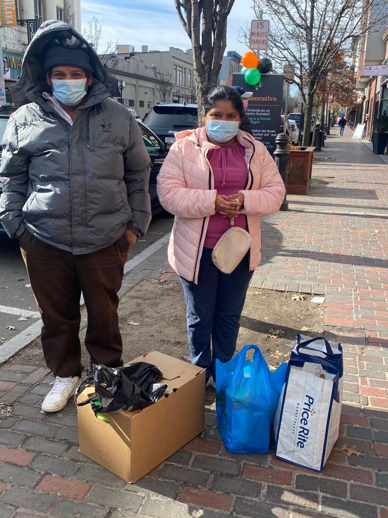 A couple stands outside with bags and boxes of supplies
