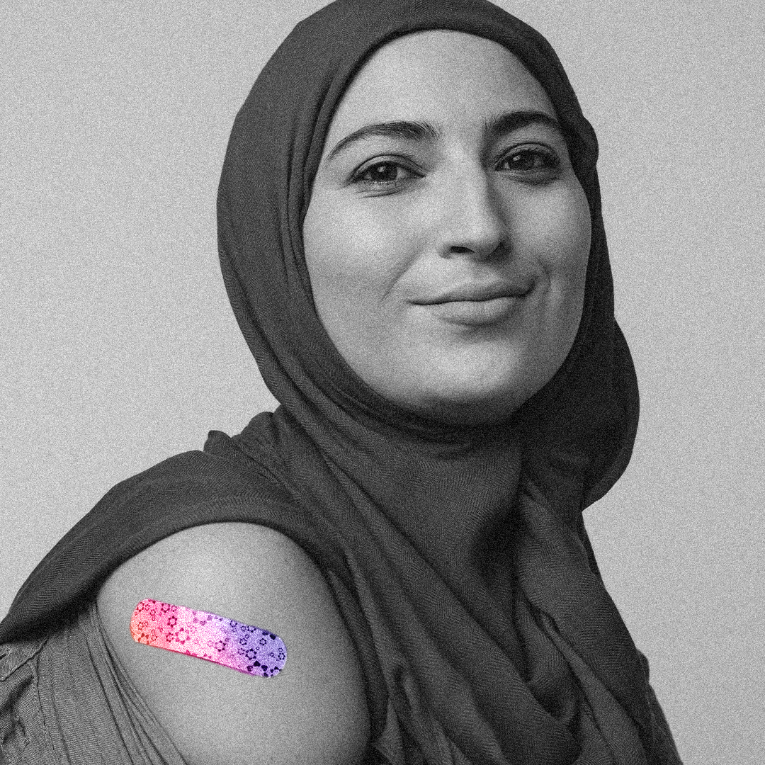Black and white photograph of a person wearing a head scarf facing camera and smiling while showing a colorized bandage on their arm