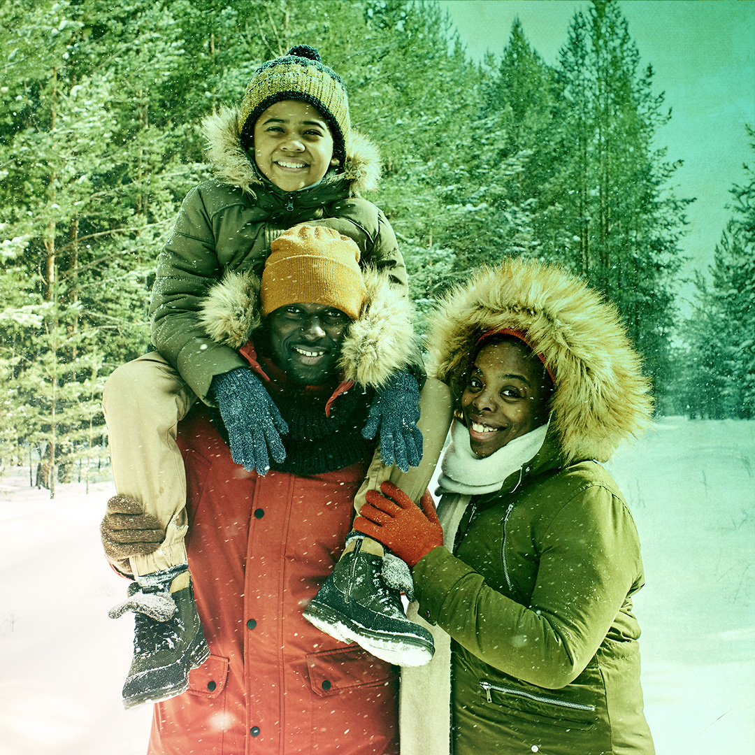 Colorized photograph of two adults in winter gear and a child sitting on shoulders of one of the adults
