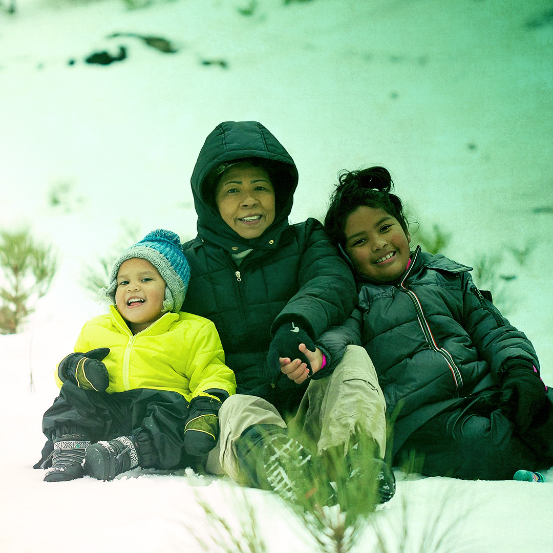 Colorized photograph of an adult and two children sitting together in winter gear on snow