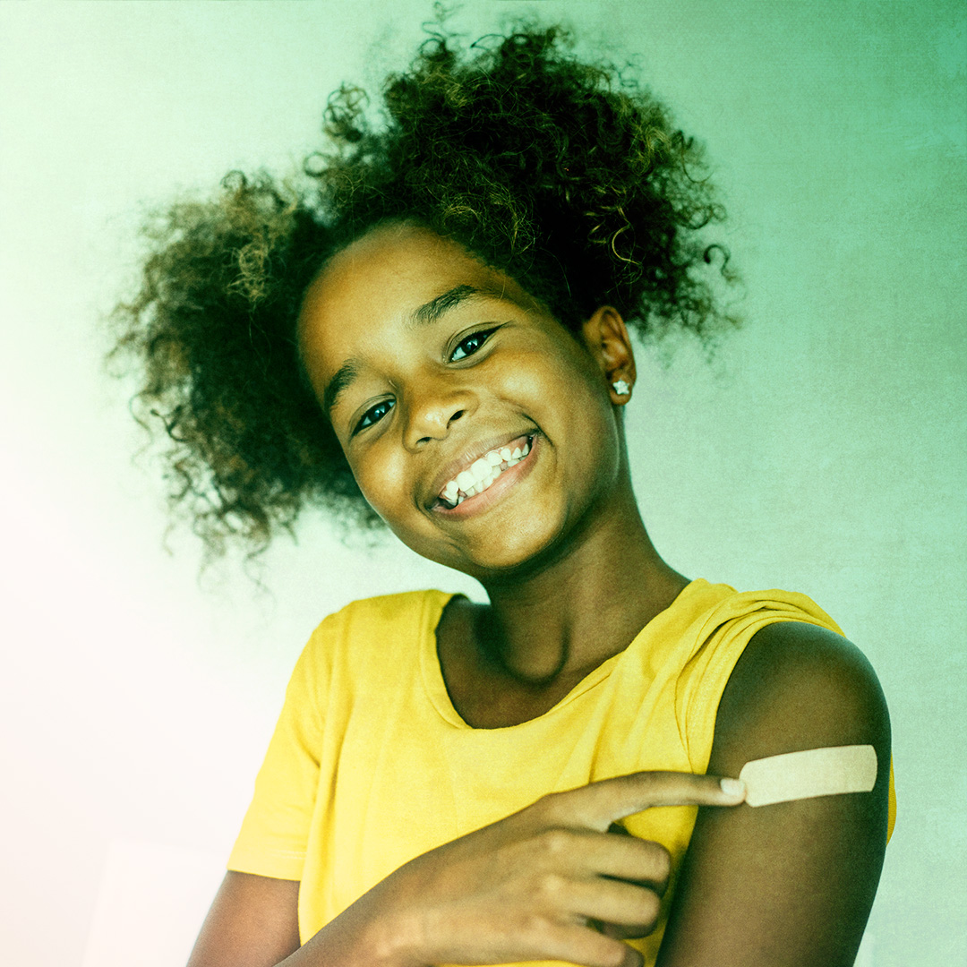 Colorized photograph of a person smiling towards the camera pointing to a bandage on their arm