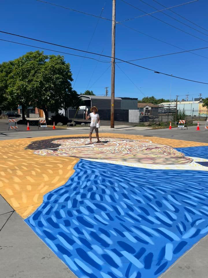 A man stands on top of a mural painted on a neighborhood street.