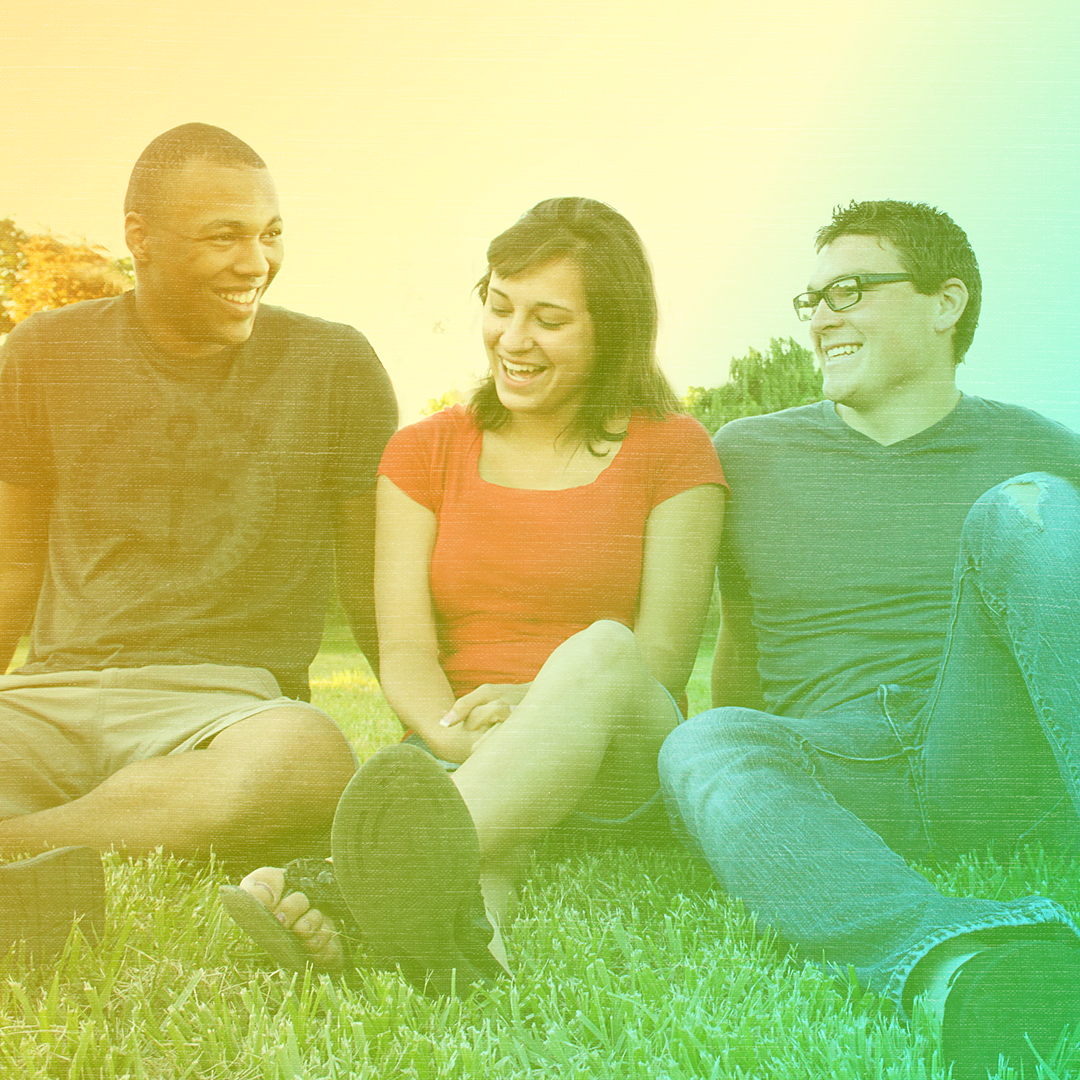 Greenish-yellow colorized photo of three people sitting on the grass smiling. A white young woman sits between a Black young man and white young man.