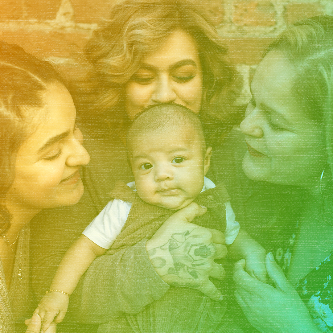 Greenish-yellow colorized photo of three women standing close together and smiling at the baby the center woman is holding.
