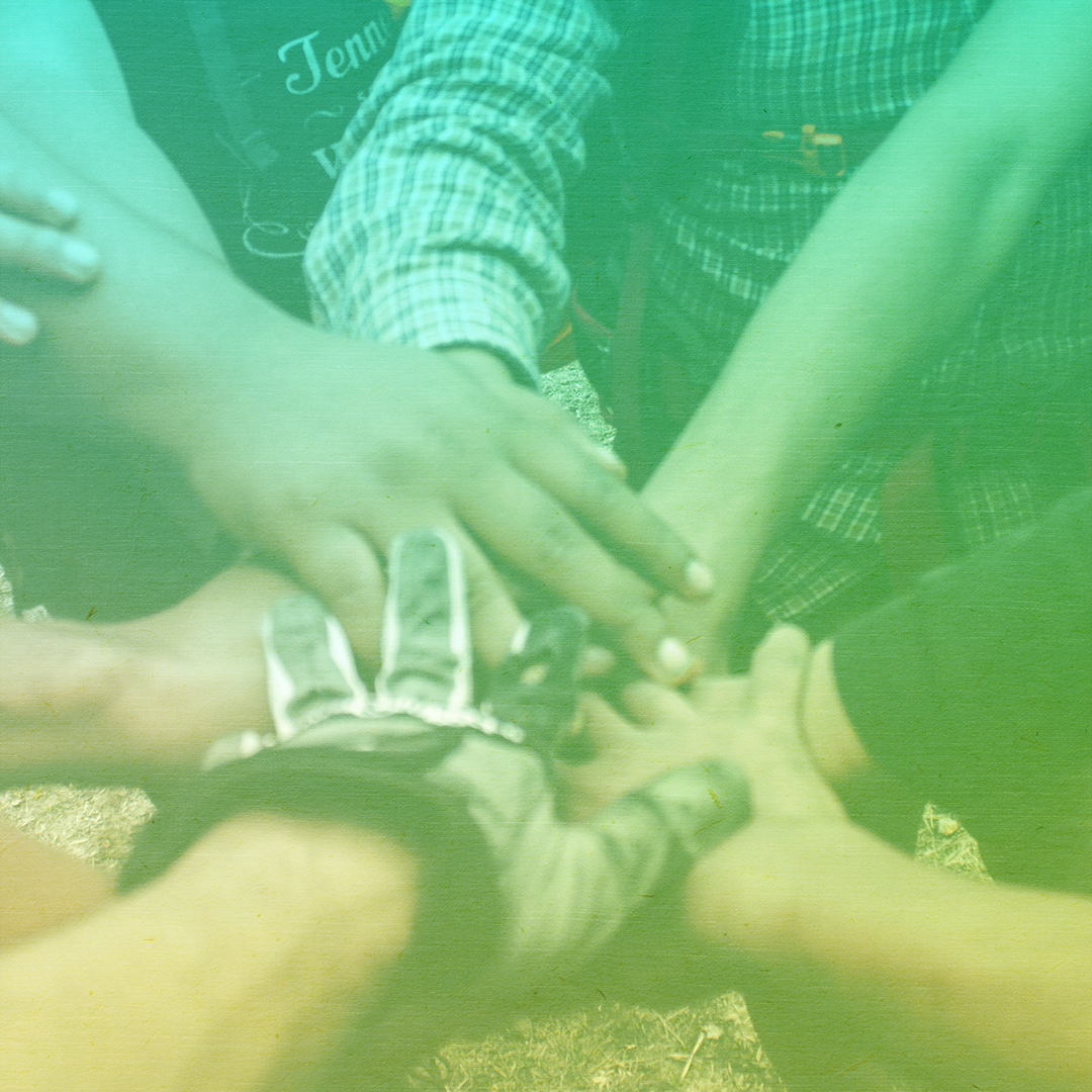 greenish-yellow filtered photo of many hands of people of different races stacked in the center