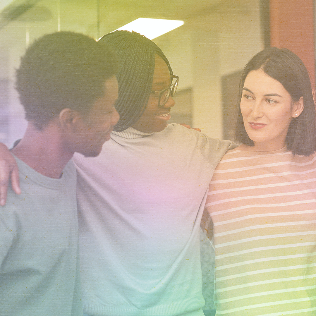 color photo of three young adults, a Black man, Black woman, and White woman with their arms around each other