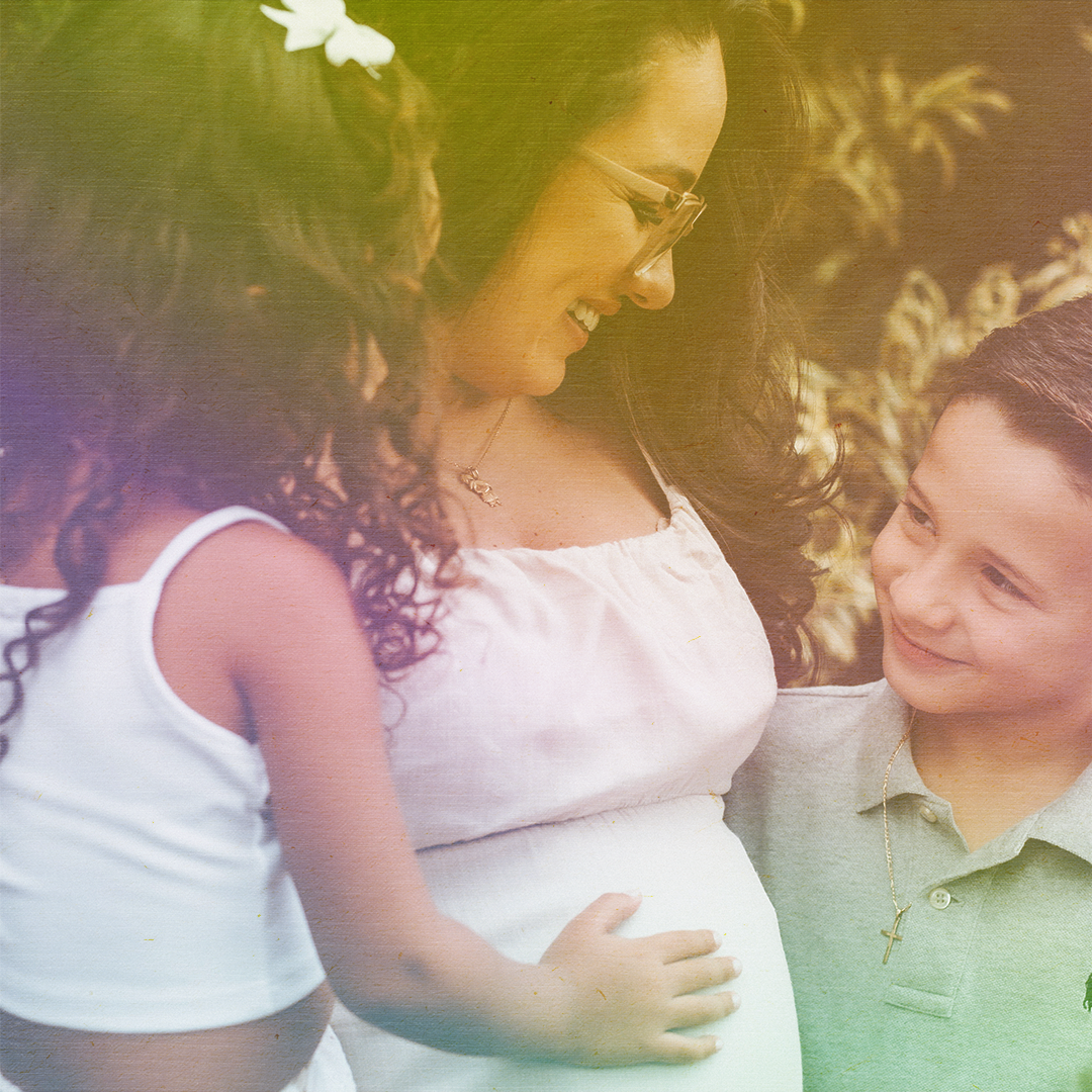 color photo of a pregnant woman embracing a boy and girl and smiling