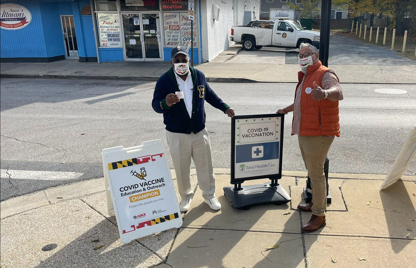 Two Black men pose next to a "free vaccination" sign and give a thumbs up