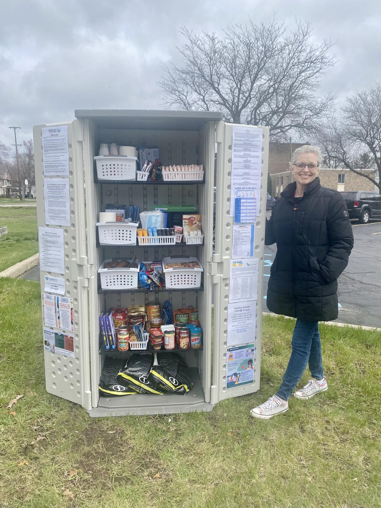 An Access Health staff member stands next to a shed filled with community pantry items. 