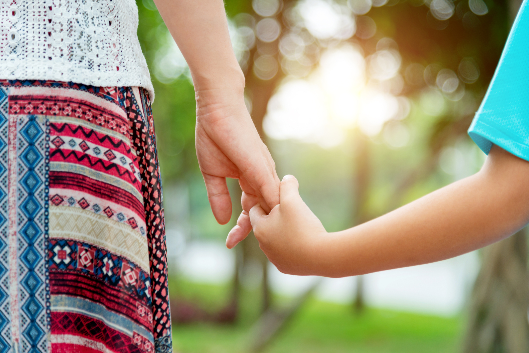 A close-up of a woman wearing a patterned skirt holding hands with a child. 