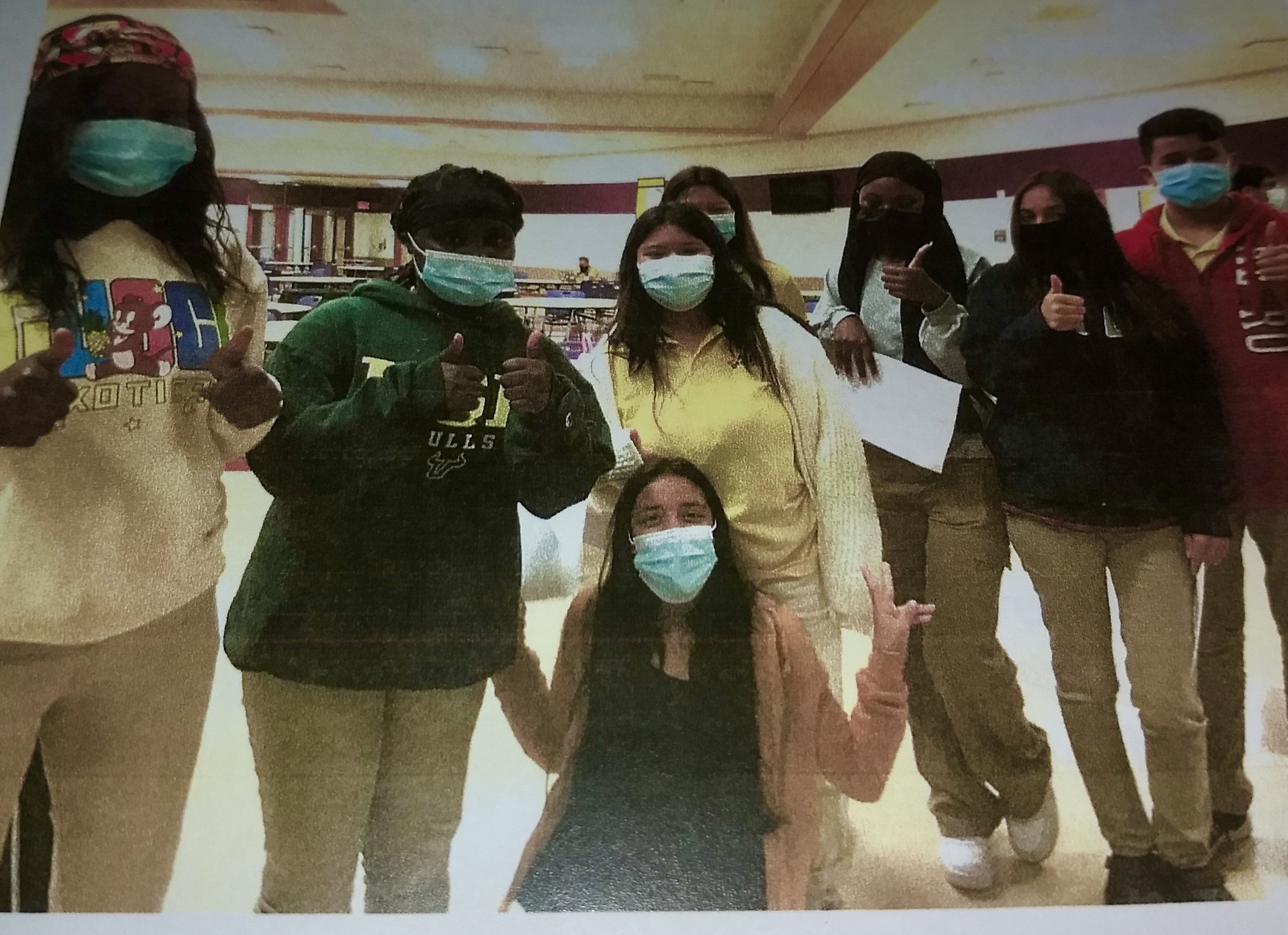 High school students wearing masks pose for a photo with their thumbs up