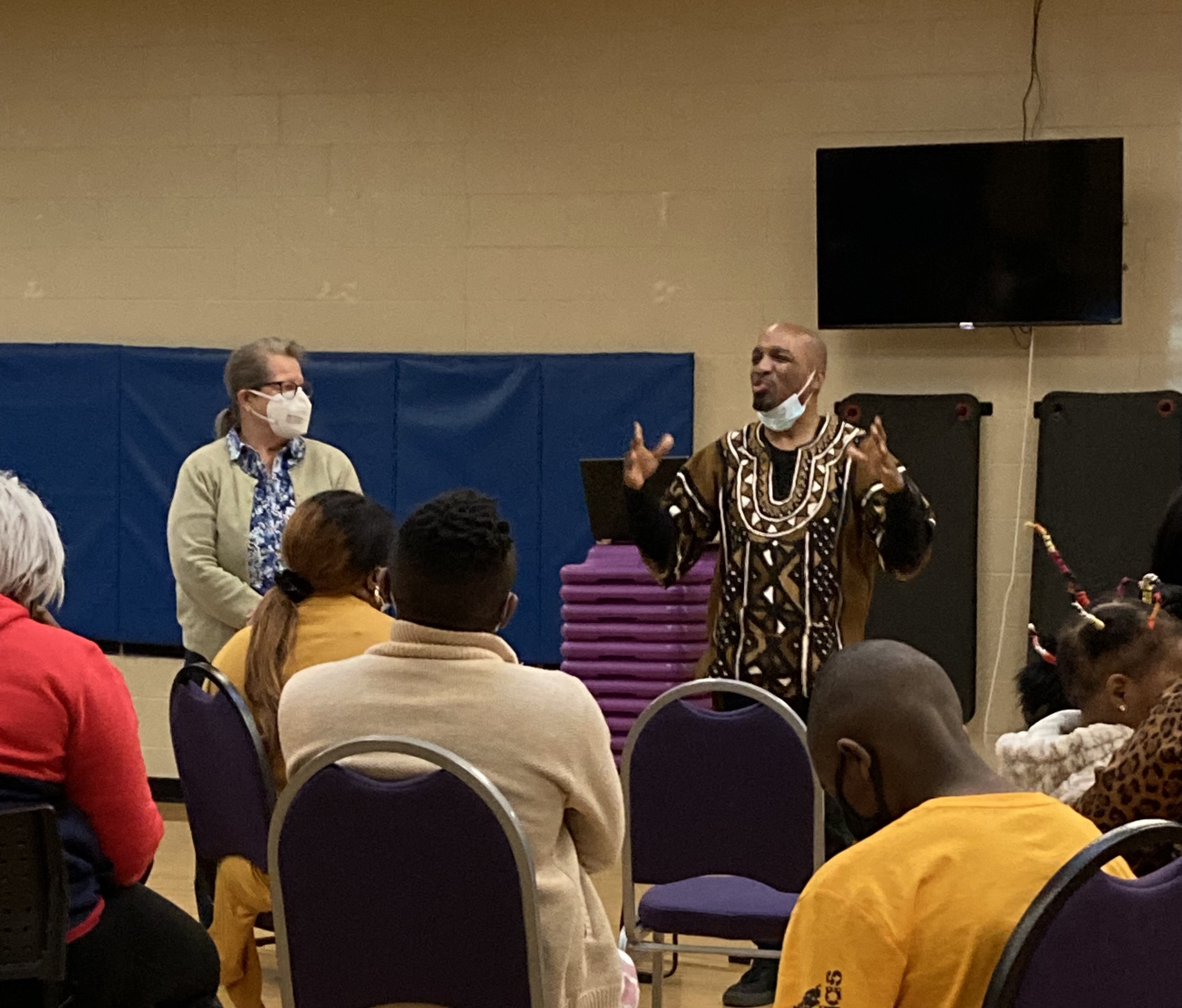A Black man speaks to an audience in a community setting