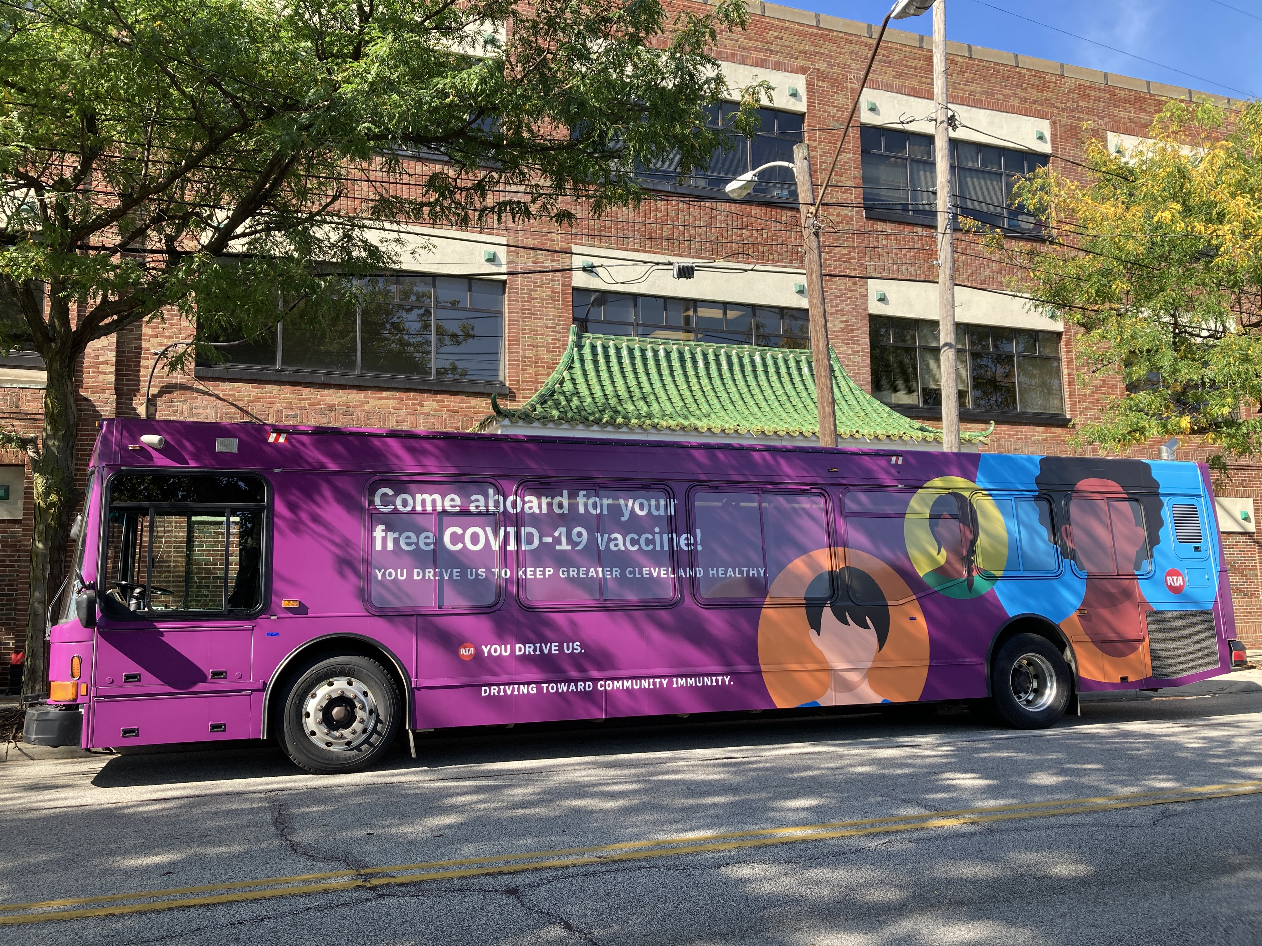 Picture of a bus painted multiple colors, featuring illustrations of people's faces, and says "Come aboard for your free vaccine"