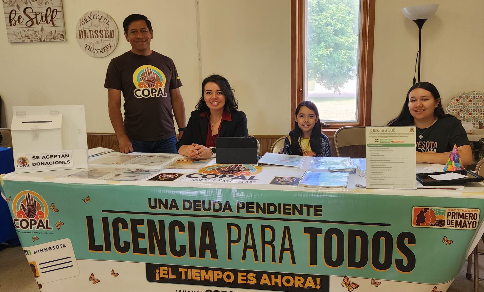 A Hispanic family sits and smiles at an information table set up in a community center