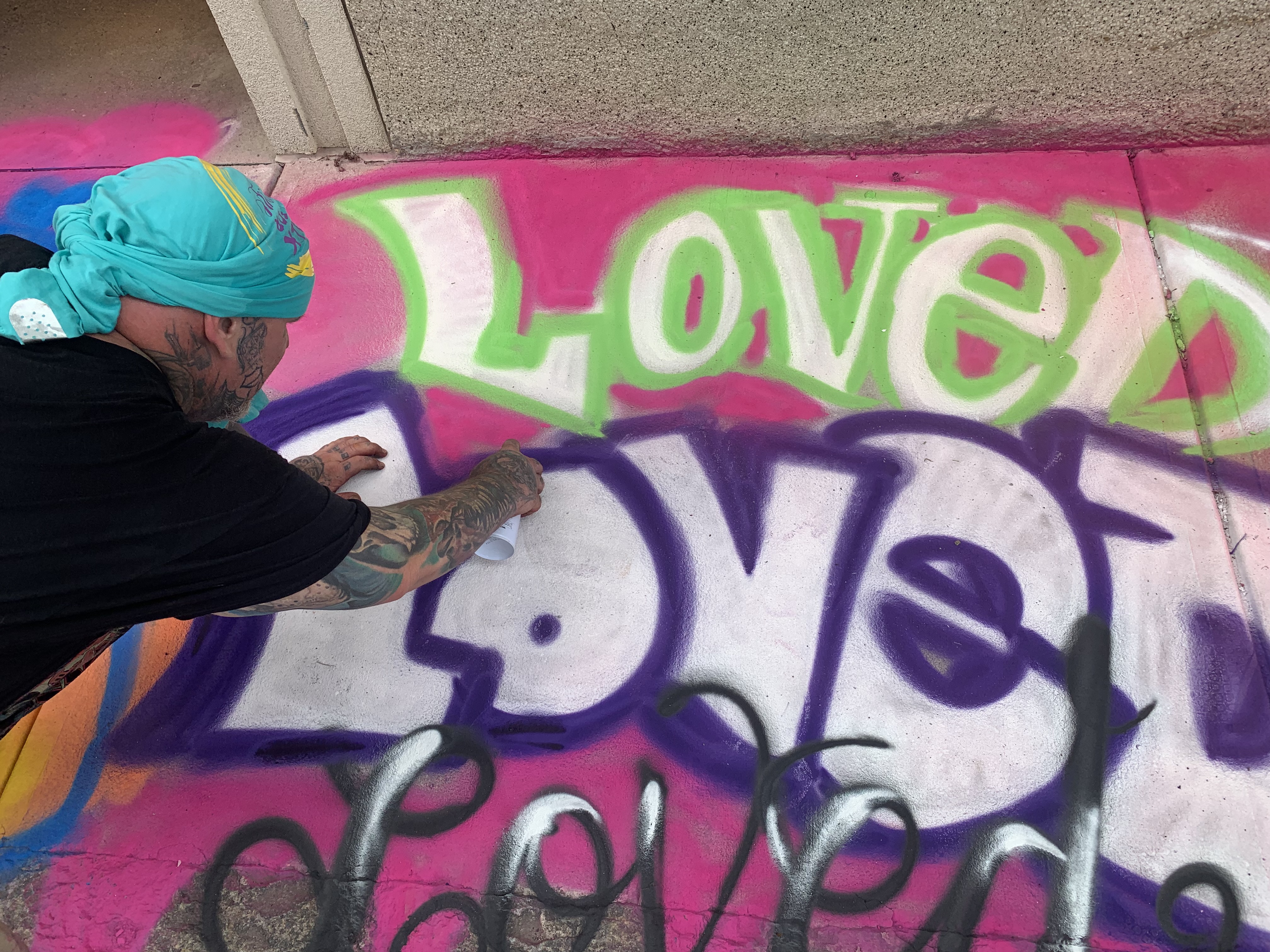 A man spray paints the word "loved" on a pink sidewalk.