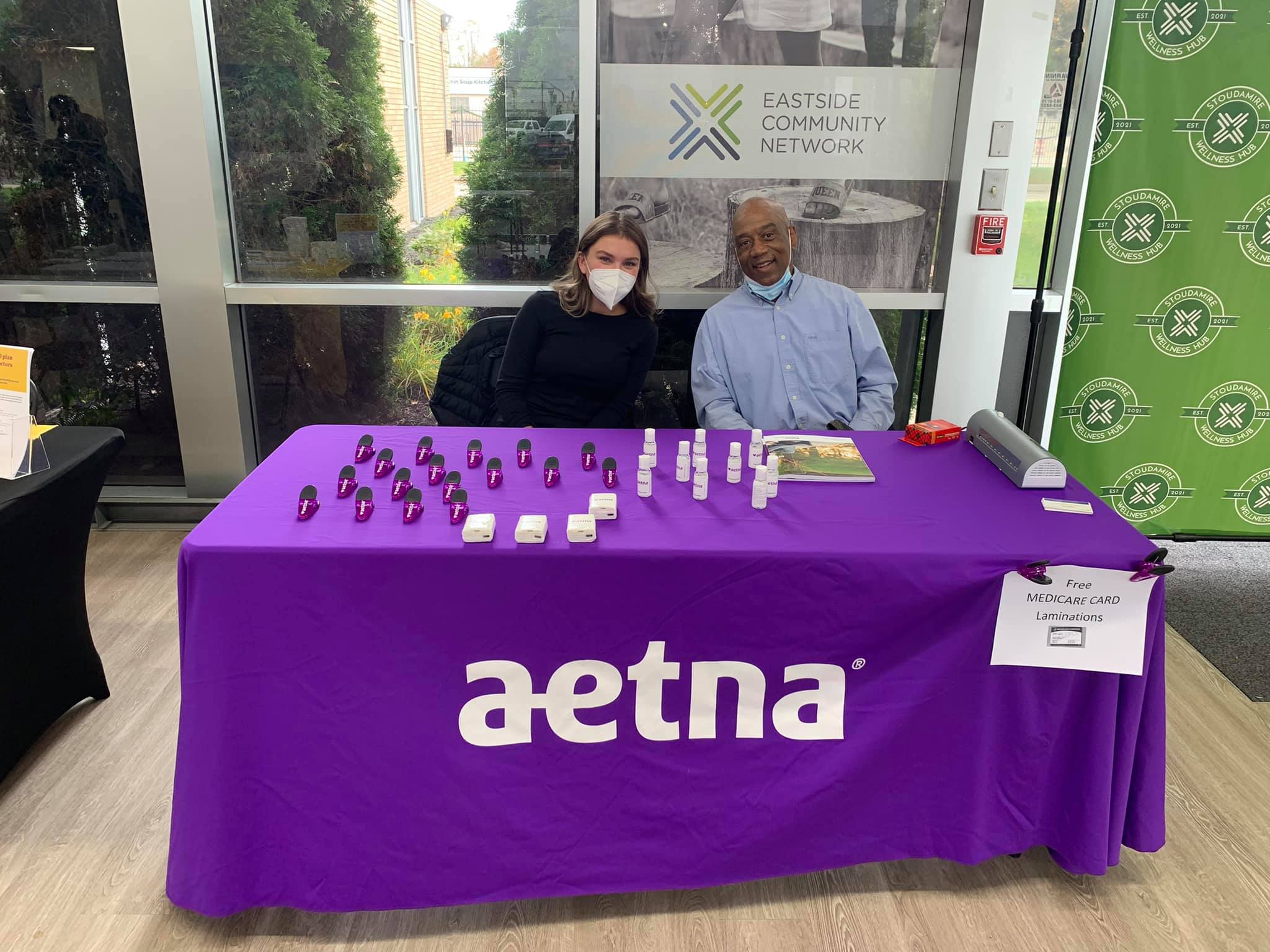 Two adults sit at an "Aetna" volunteer table 