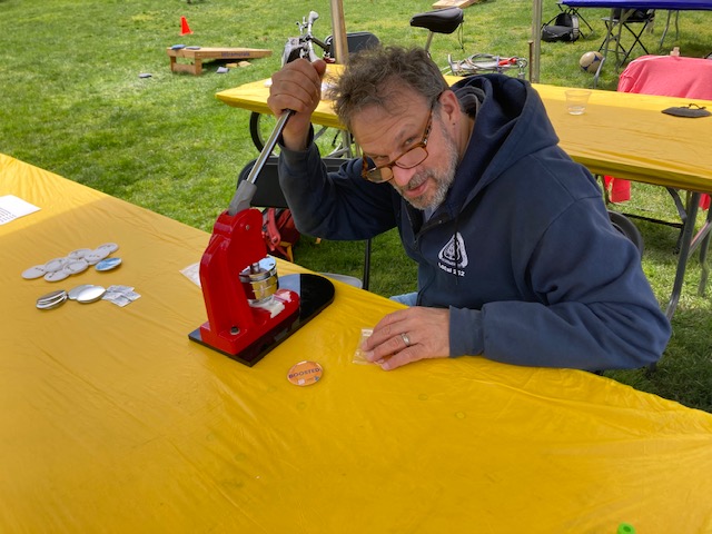 A man sits at a table and makes buttons for a community event 
