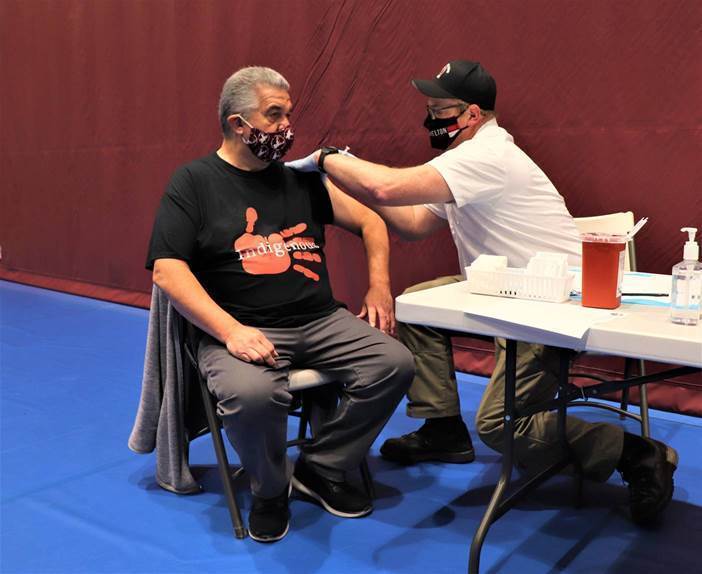 A man wearing a mask sits in a chair and receives his COVID vaccine
