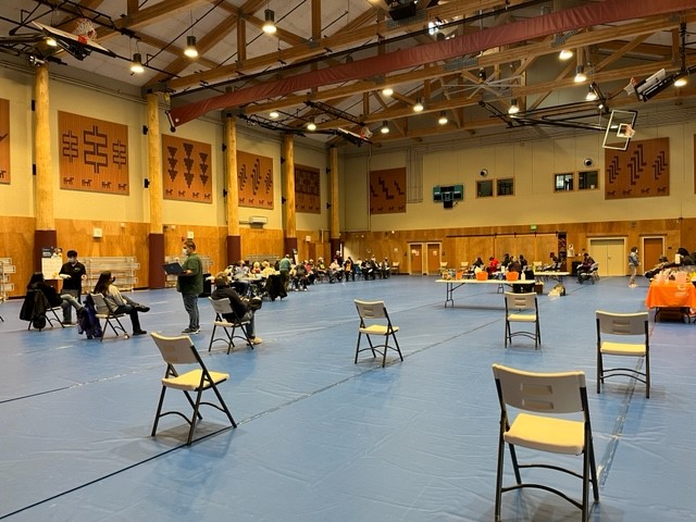 A gymnasium is filled with people sitting in chairs, and empty chairs