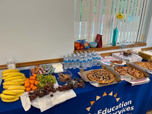 Snacks including fruit, water, and pizza are set up at a table with a blue tablecloth