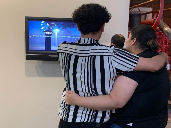 Two students embrace in front of a video art piece