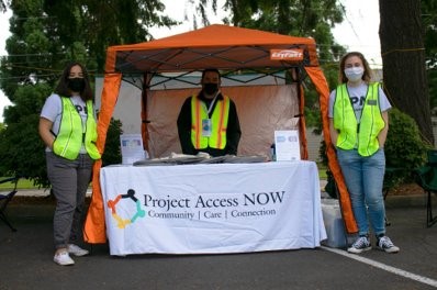 Three volunteers wearing bright green vests stand in front of a registration table
