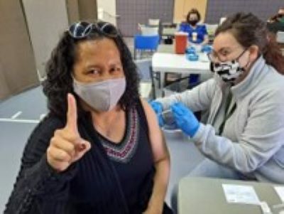 A woman receives a vaccine and holds up a #1 sign. 