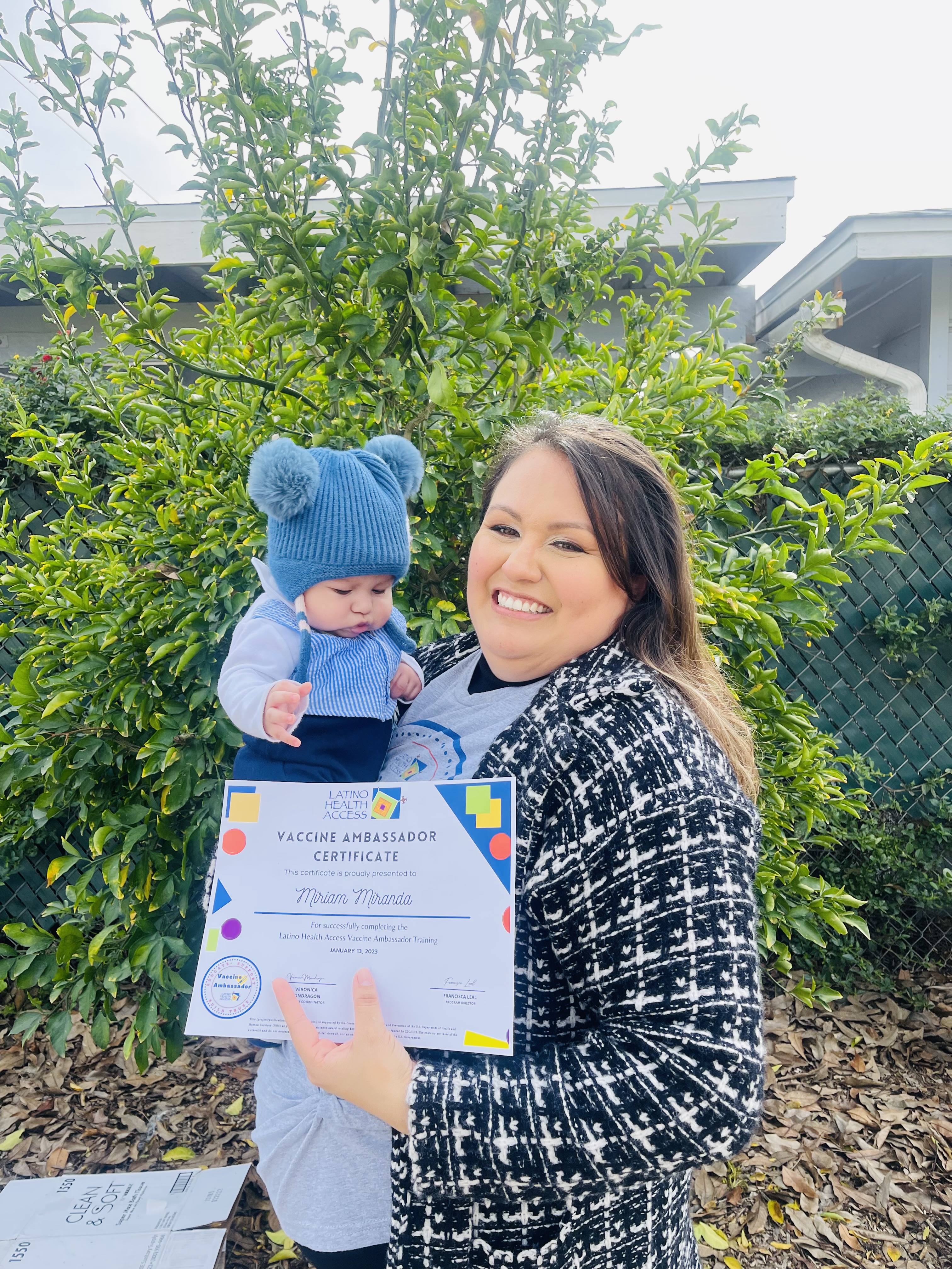A mother holds her baby and also holds a vaccine ambassador certificate