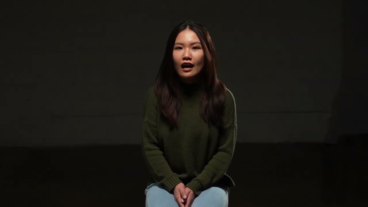 An Asian woman wearing a green sweater is speaking. 