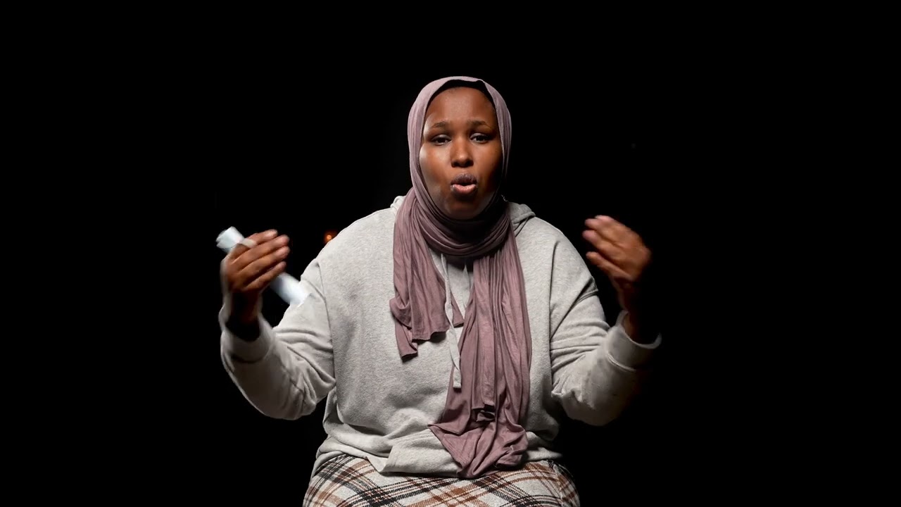 A Black woman wearing a sweater and headscarf is speaking. 