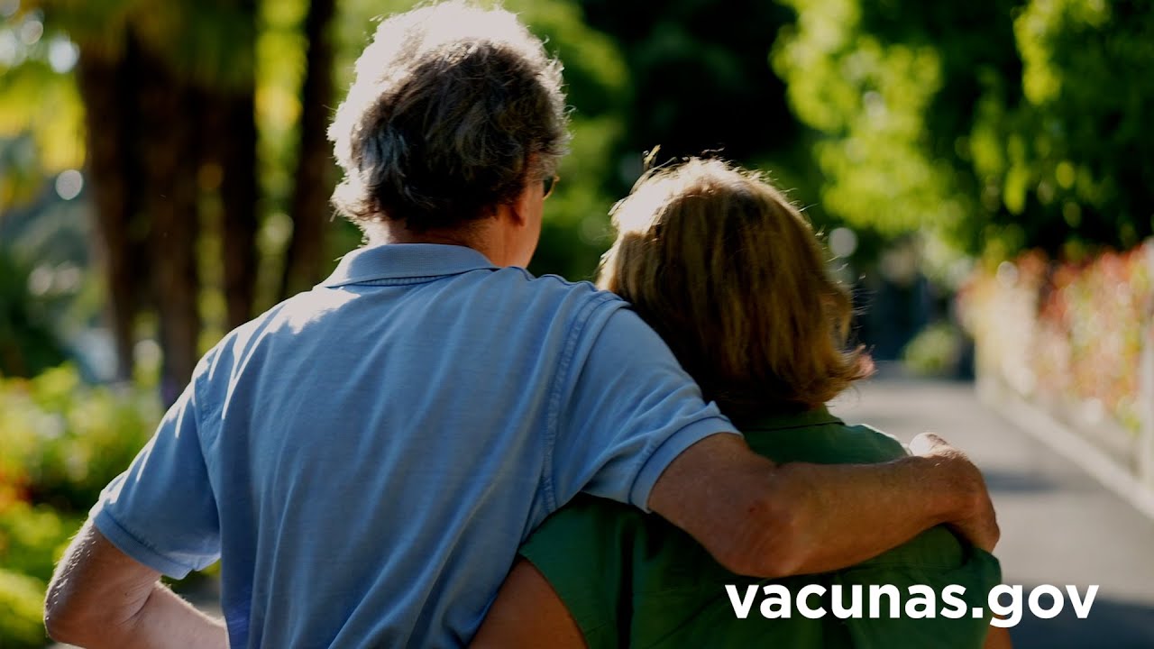 A view from the back of two older adults embracing on a walk outdoors. 