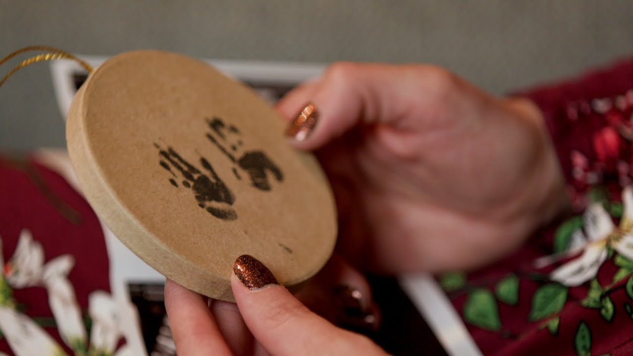 Image of a woman's hands holding a circular wooden ornament with a baby's hand prints.