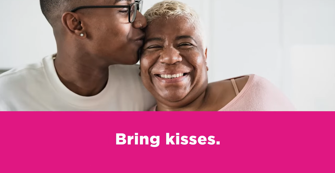 Black woman hugging and kissing older, smiling Black woman on the forehead.