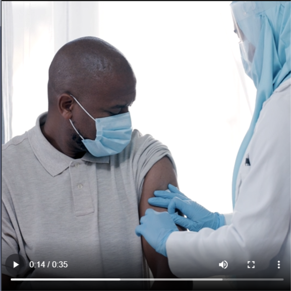 black male wearing a mask, looking down at his arm as a healthcare worker places an adhesive bandage on it. 