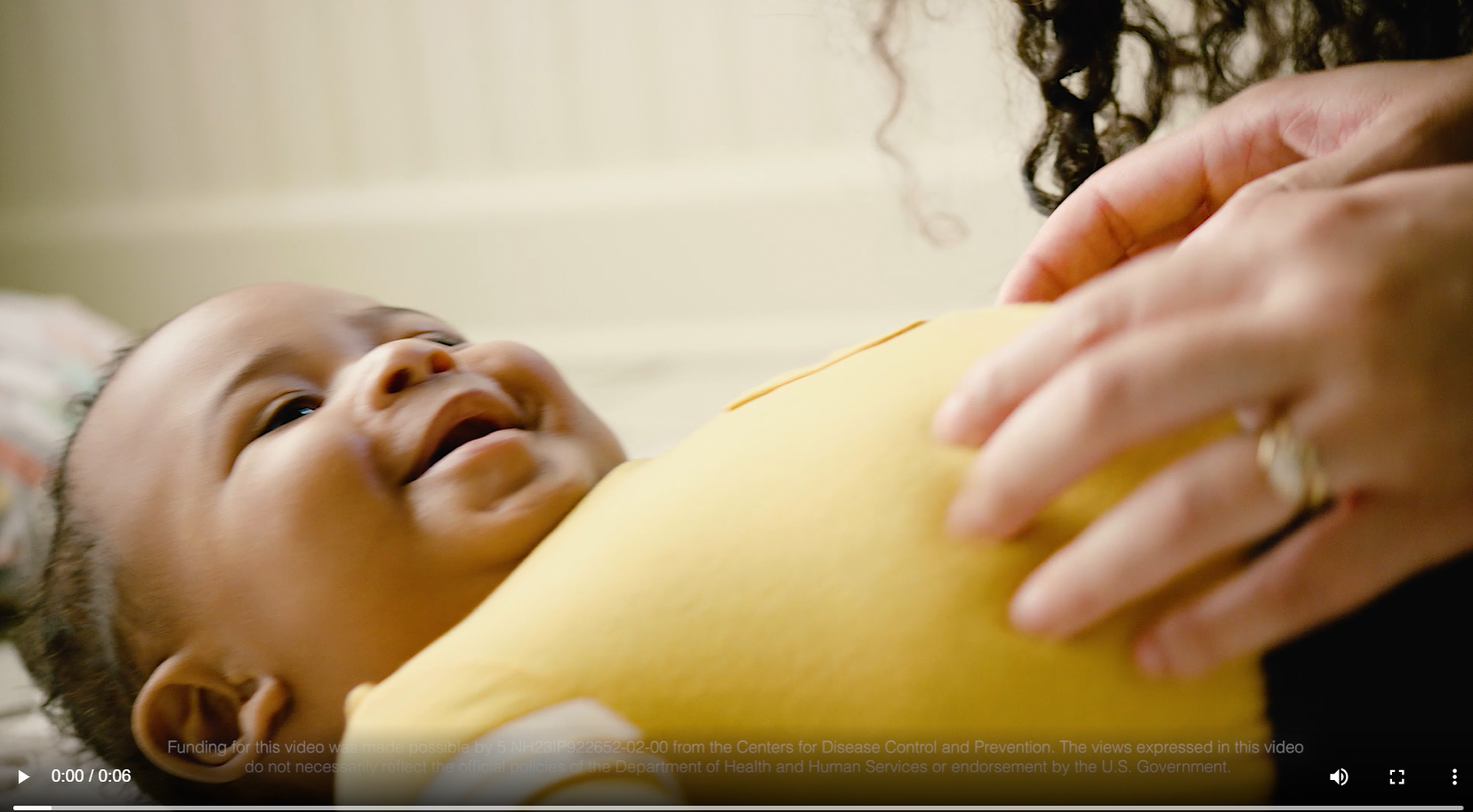 An African American baby smiles while his mom rubs his stomach