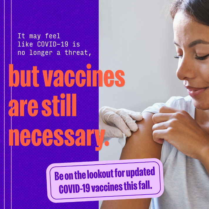 A Latina woman in profile smiles and rolls up her shirt sleeve, while a gloved hand cleans her upper shoulder ahead of getting vaccinated.