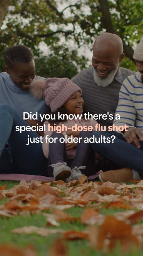 Video still shows a young Black girl with a huge smile sitting alongside older family members in the grass covered with autumn leaves.