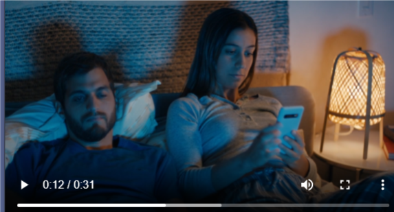 Scene from a video showing a man and woman going to bed. The woman is looking at her phone.