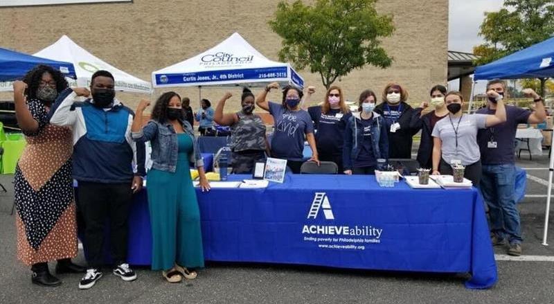 A crowd of people wearing masks do a muscle pose while standing around a table at a
