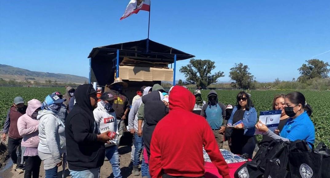 A group of people watch a volunteer present information from a flyer about vaccines