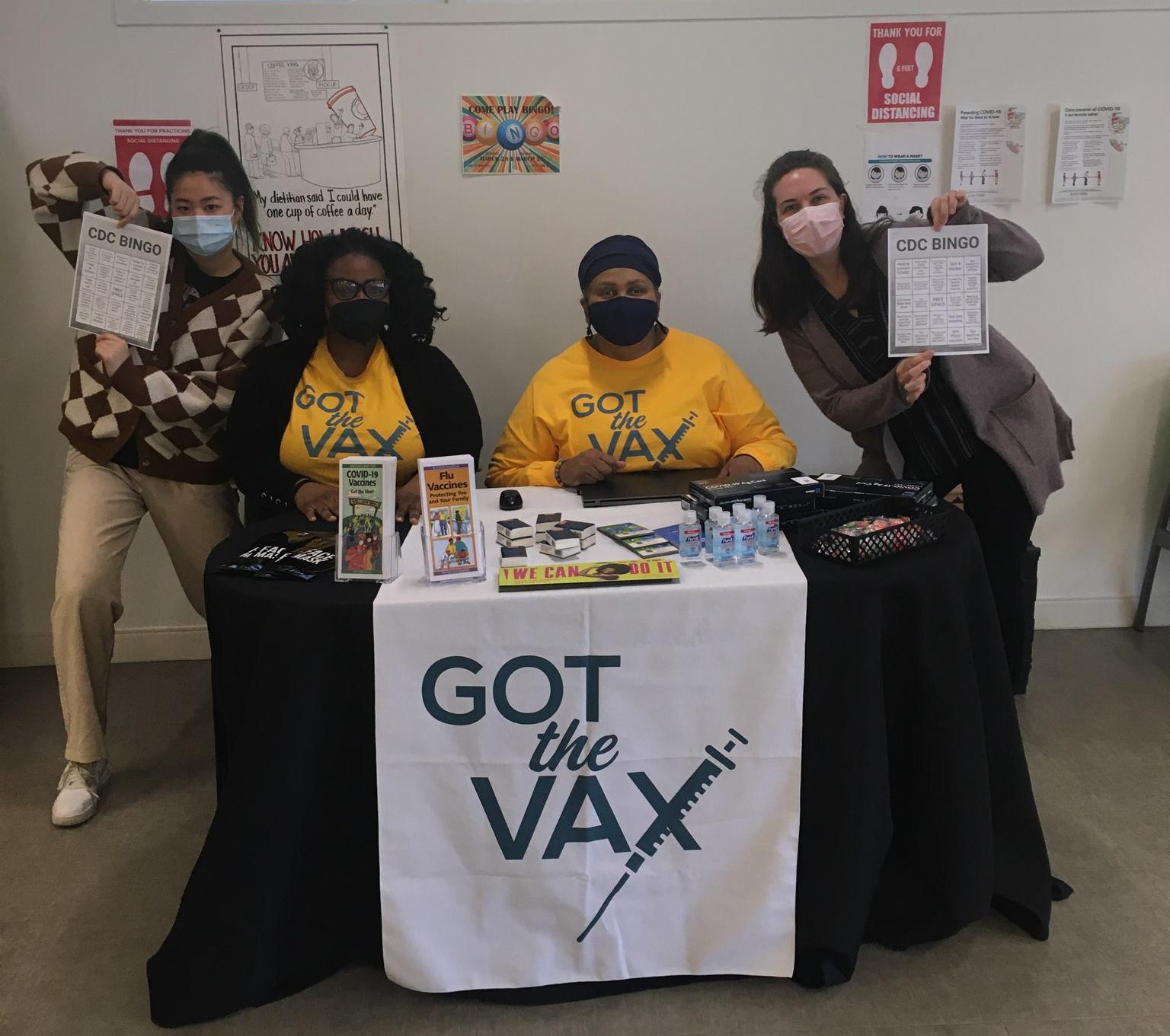 Volunteers pose behind a "Got the Vax" table showing off CDC Bingo cards