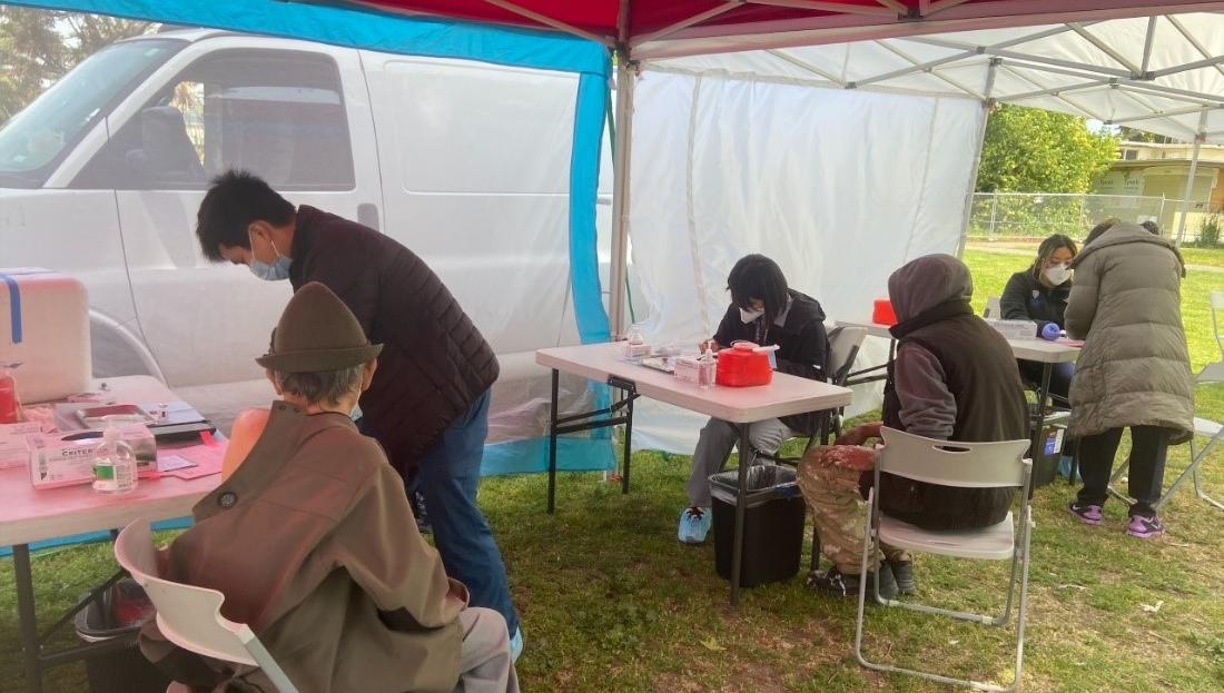 Three patients sit at vaccination stations in a tent at a vaccine event