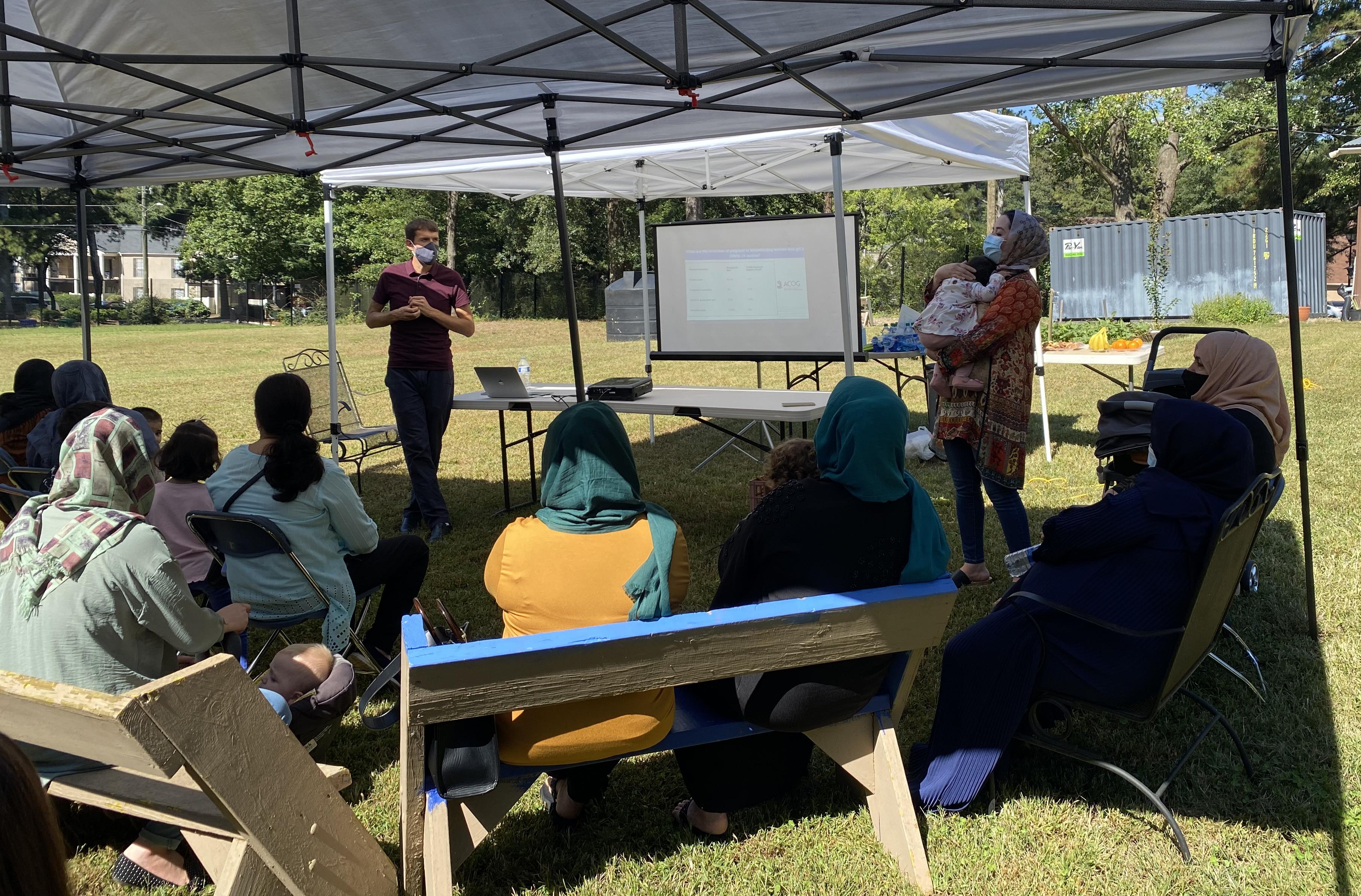A crowd listens to an outdoor presentation for a Friends of Refugees event.