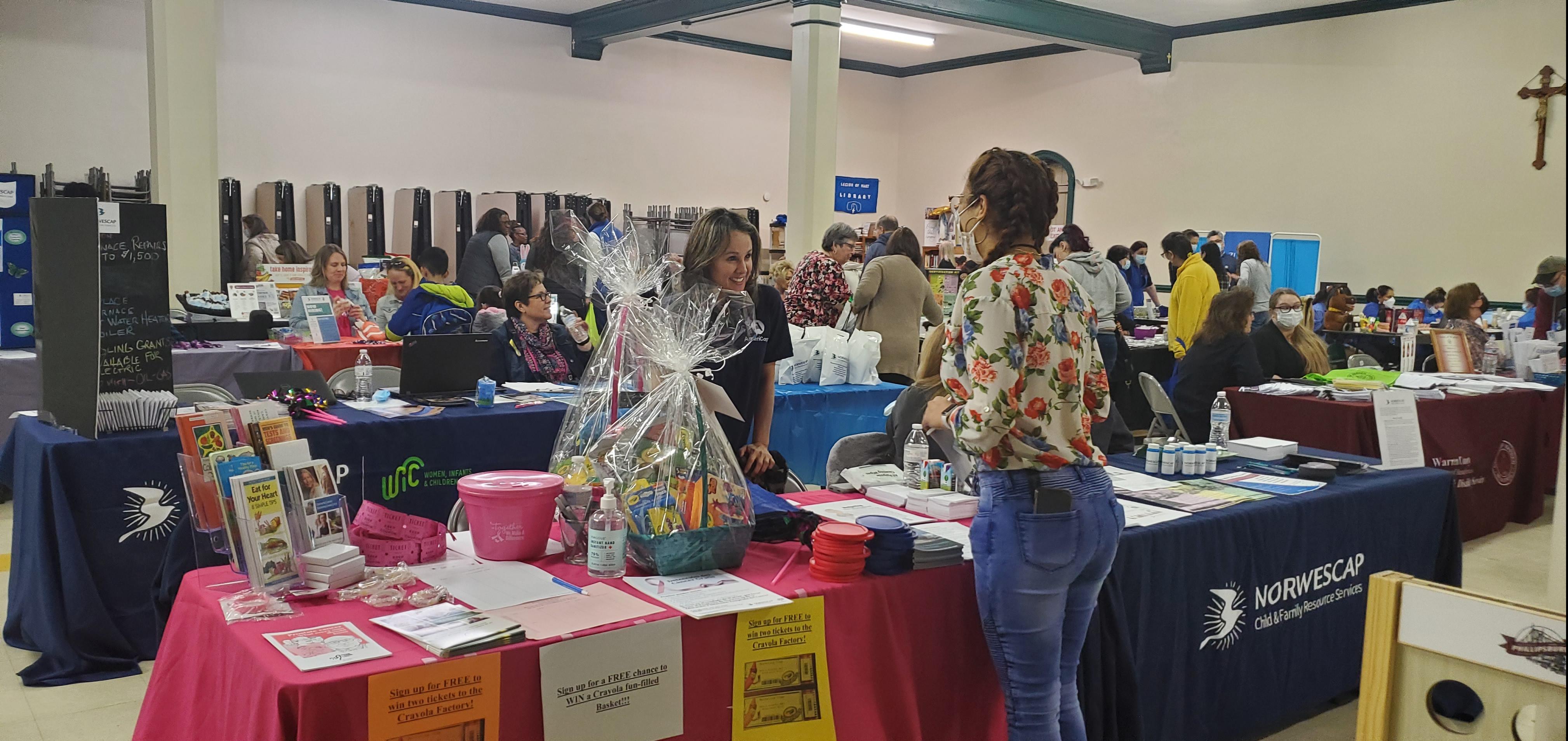 A woman volunteer at a table smiles and greets another woman